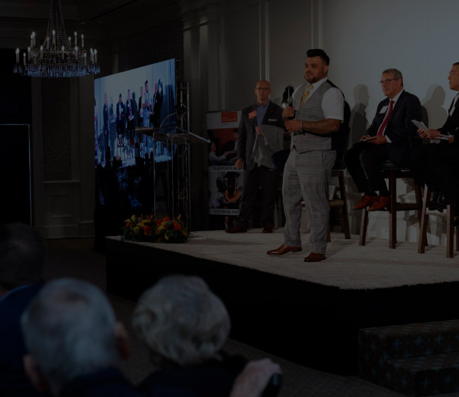 Man presenting on stage during a business event with panelists and audience