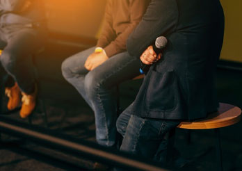 Panelists seated on stools during an event, with one person holding a microphone, prepared to speak.