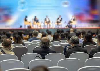 Audience seated in a conference hall watching a panel discussion on stage.