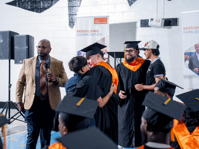 PEP graduates in caps and gowns embrace loved ones during a Prison Entrepreneurship Program graduation ceremony focused on restoring families and rebuilding communities