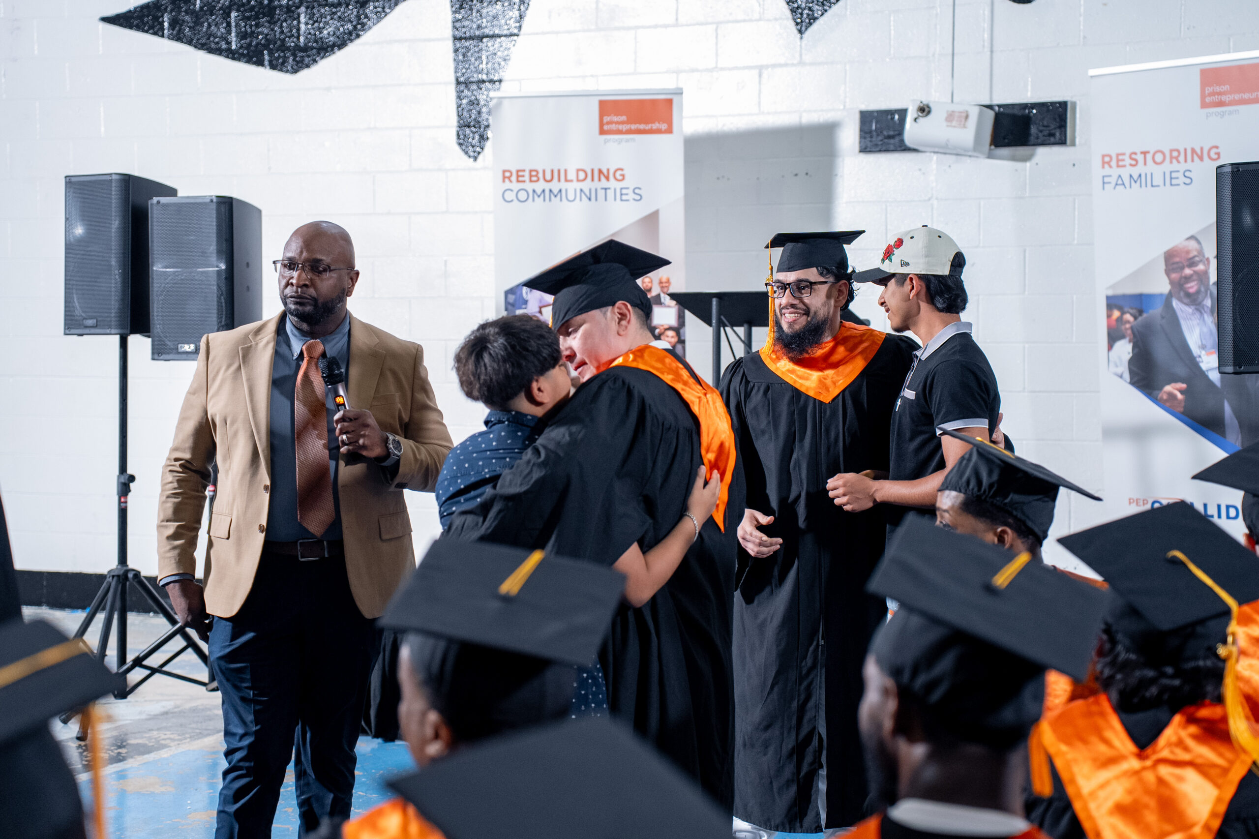 PEP graduates in caps and gowns embrace loved ones during a Prison Entrepreneurship Program graduation ceremony focused on restoring families and rebuilding communities