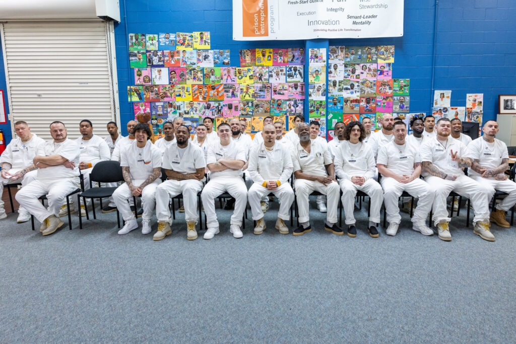 PEP participants seated together at a graduation event, smiling in front of a colorful wall of vision boards that reflect their goals and personal growth