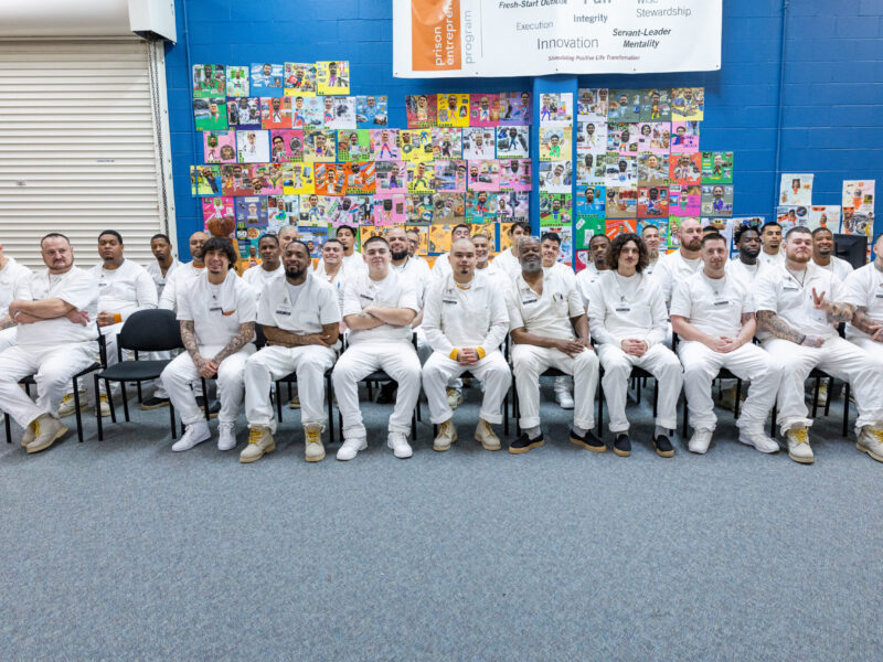 PEP participants seated together at a graduation event, smiling in front of a colorful wall of vision boards that reflect their goals and personal growth