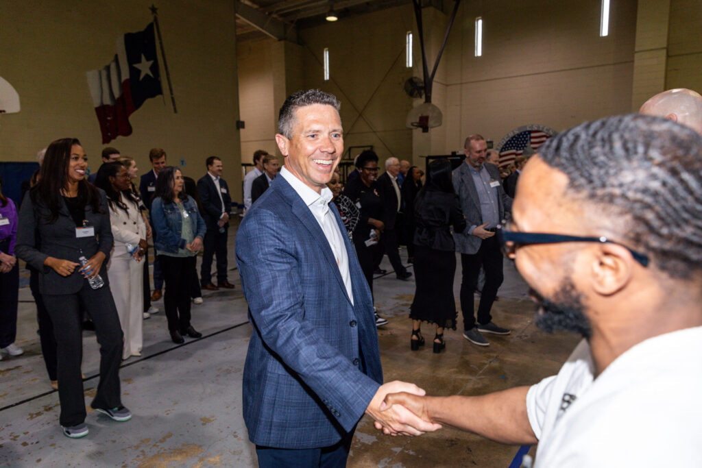 Business leader shakes hands with PEP participant during a Prison Entrepreneurship Program event inside a Texas prison gym, fostering mentorship and connection
