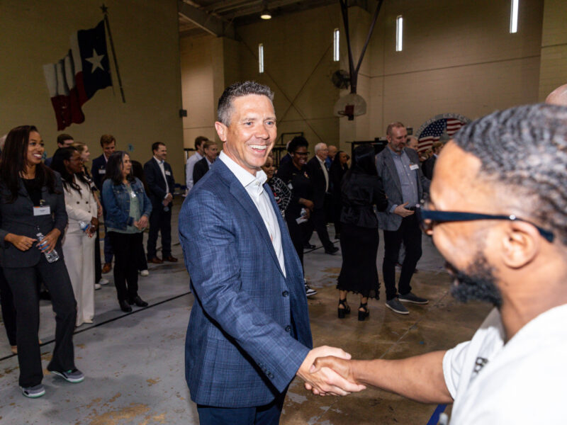 Business leader shakes hands with PEP participant during a Prison Entrepreneurship Program event inside a Texas prison gym, fostering mentorship and connection
