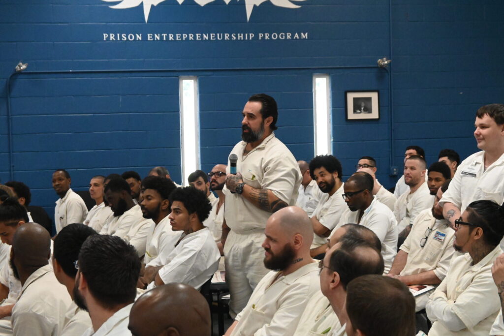 Incarcerated man participating in a Prison Entrepreneurship Program event, standing and speaking into a microphone during a session with fellow PEP participants