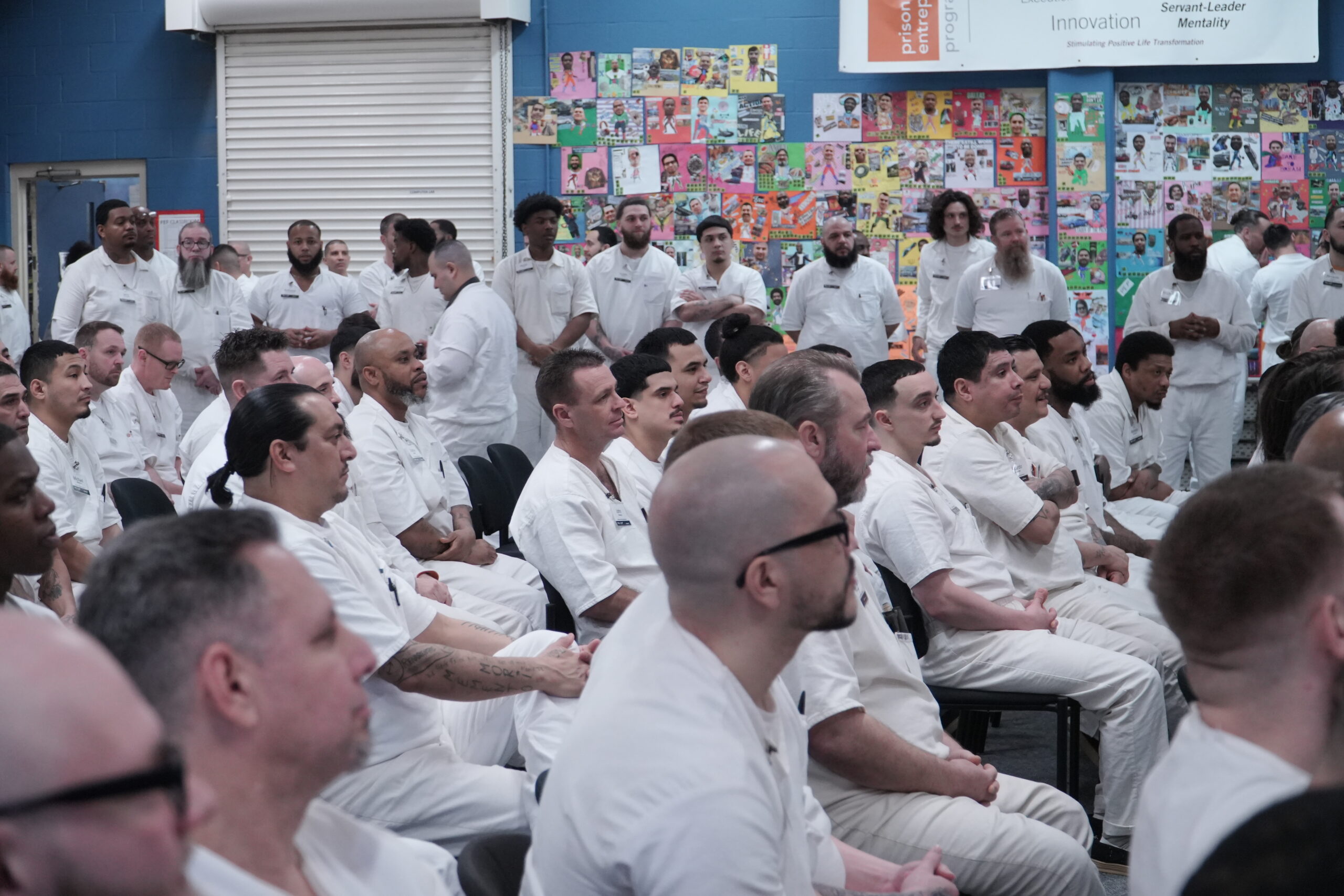PEP participants seated and standing attentively during a classroom session, with colorful vision boards and program values displayed on the wall