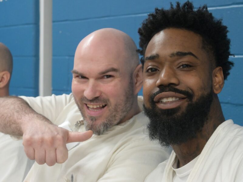 Two Prison Entrepreneurship Program participants smile and pose during a PEP class session inside a Texas correctional facility