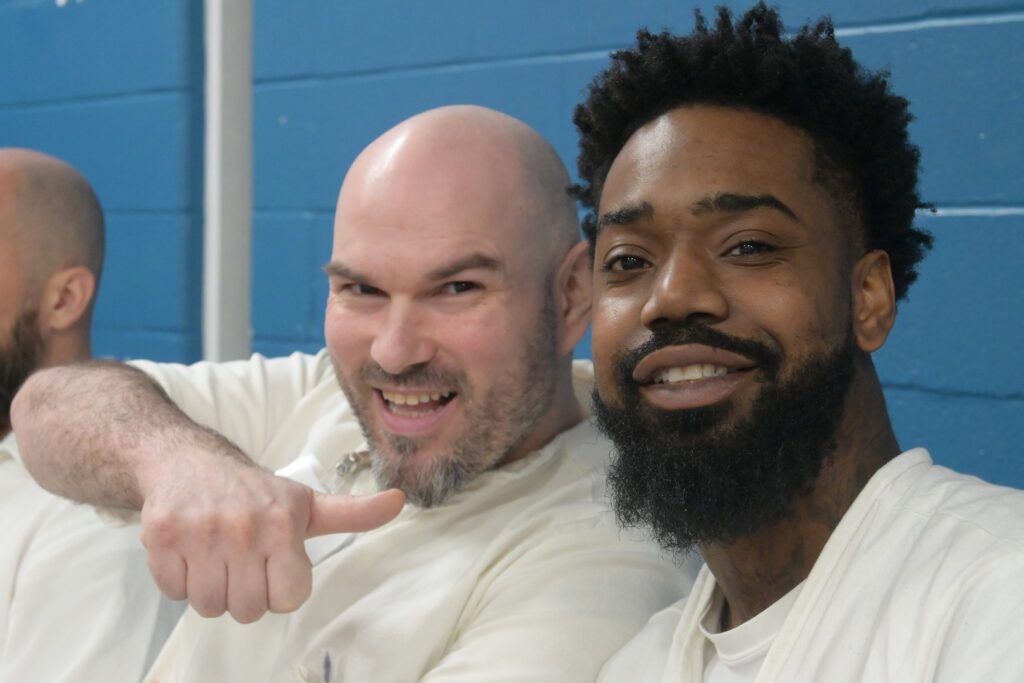 Two Prison Entrepreneurship Program participants smile and pose during a PEP class session inside a Texas correctional facility