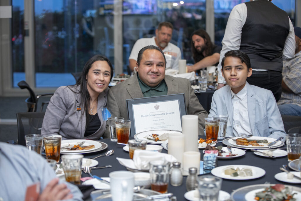 PEP graduate celebrates with family at Prison Entrepreneurship Program graduation dinner while holding his framed diploma