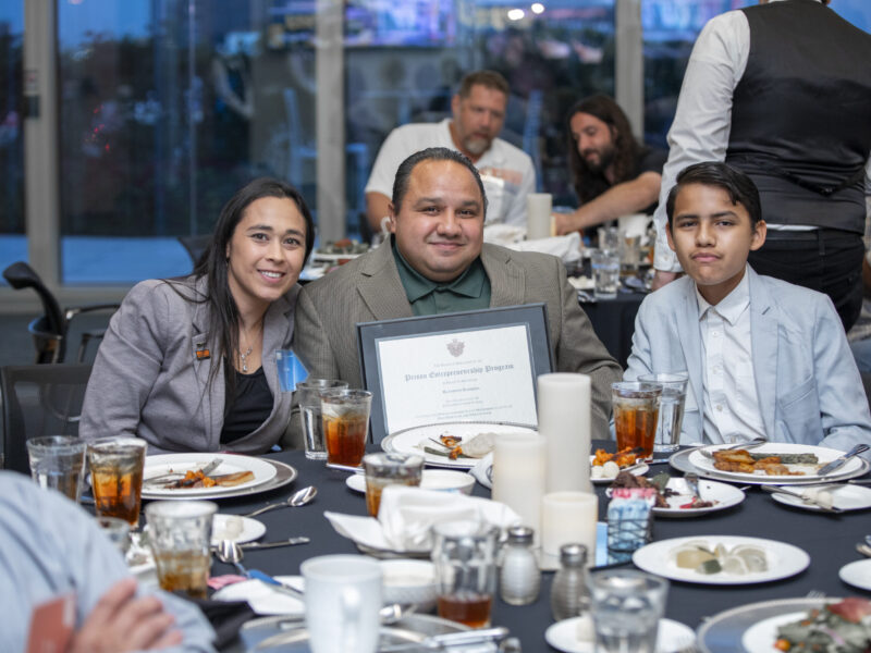 PEP graduate celebrates with family at Prison Entrepreneurship Program graduation dinner while holding his framed diploma