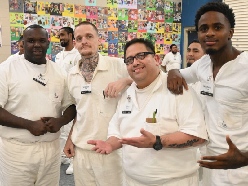 Prison Entrepreneurship Program participants gather and pose in front of colorful artwork during a PEP class session celebrating creativity and community